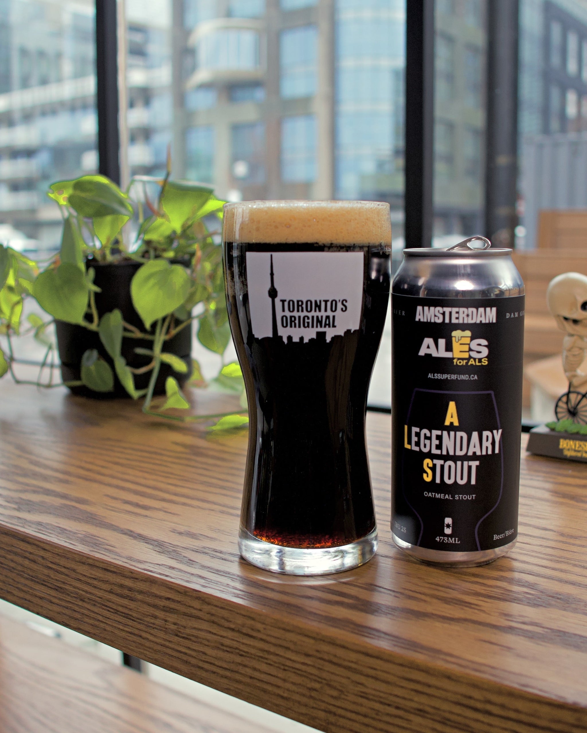 Glass of dark beer and can labeled 'Legendary Stout' on a wooden surface with a cityscape in the background.