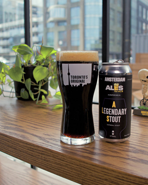 Glass of dark beer and can labeled 'Legendary Stout' on a wooden surface with a cityscape in the background.