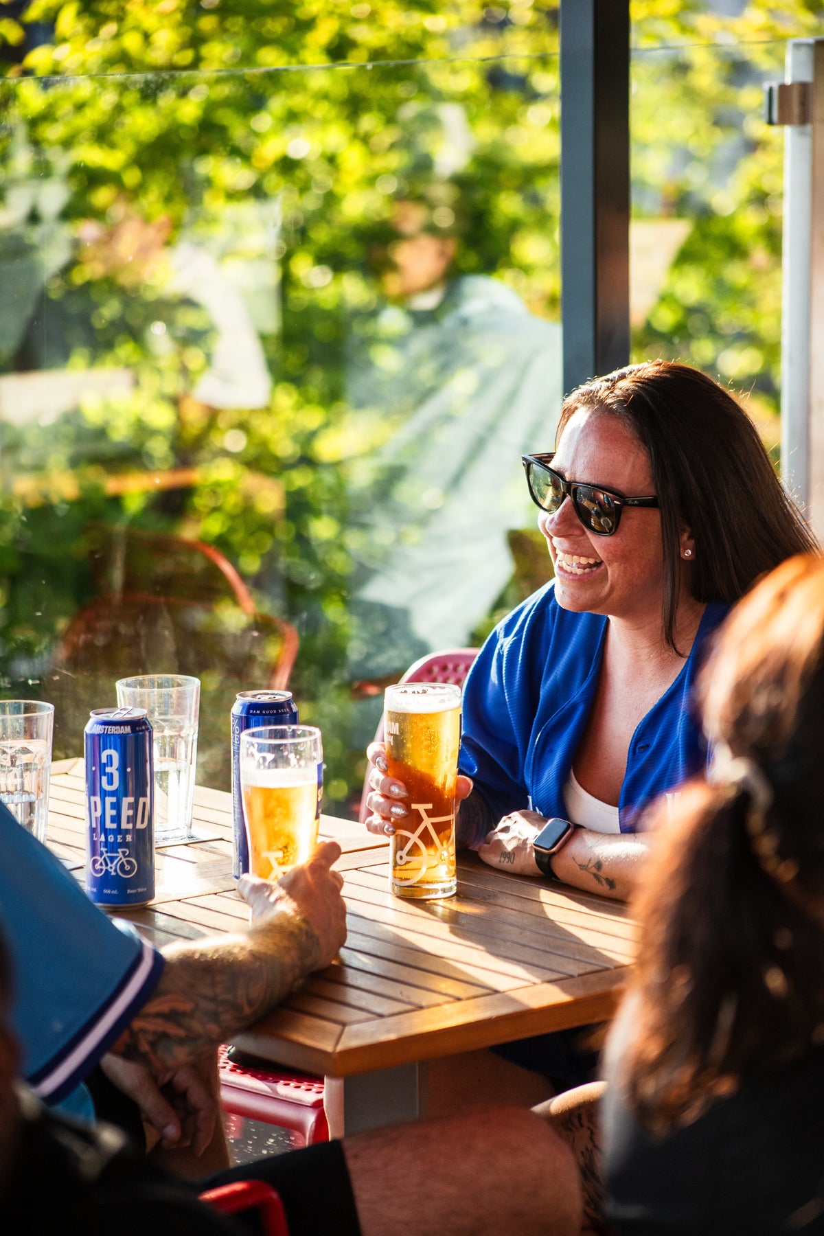 Woman in a Blue Jays jersey sitting at an outdoor table with drinks, surrounded by greenery